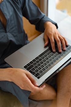 A close-up shot of a man using a laptop indoors, showcasing casual work-from-home setup.