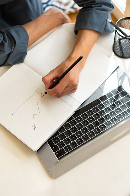 Person drawing a zigzag graph on a notebook placed atop a laptop; ideal for business or analysis themes.