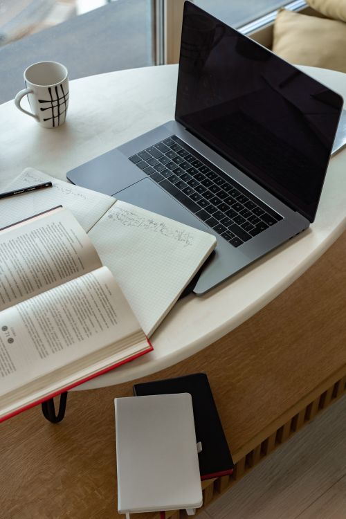 Free A cozy indoor workspace featuring a laptop, open book, notepad, and coffee, perfect for studying or remote work. Stock Photo