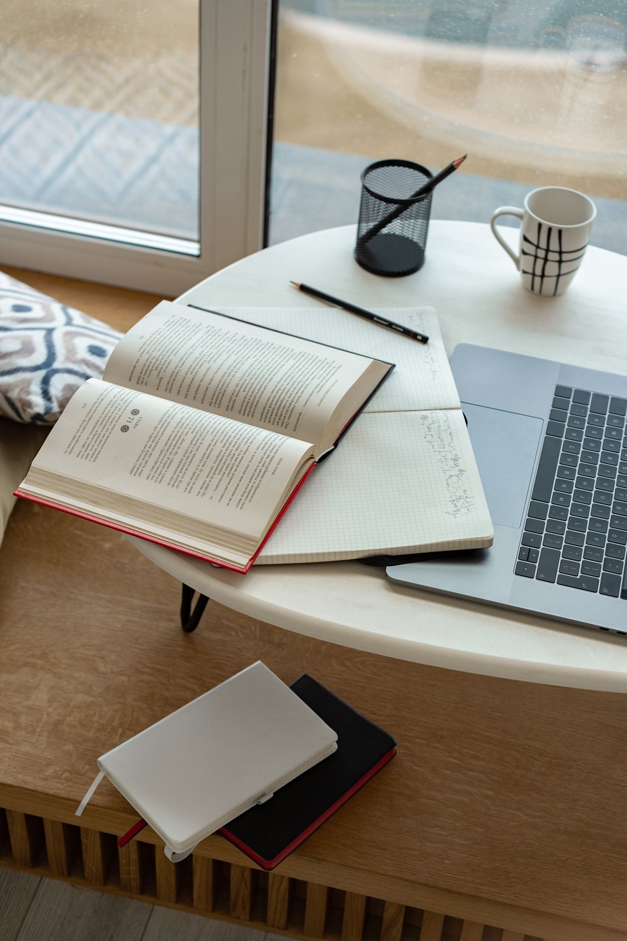 A cozy indoor study setup with an open notebook, laptop, and coffee mug by a window — student study break setup