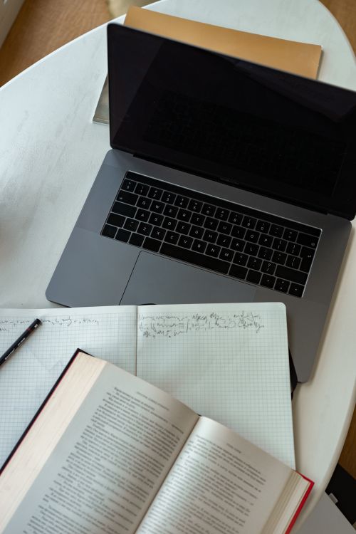 Free Overhead shot of a laptop, open book, and notebook on a wooden table. Stock Photo