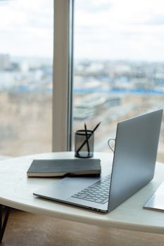 A sleek laptop and notebook on a bright workspace table by a window with city view.