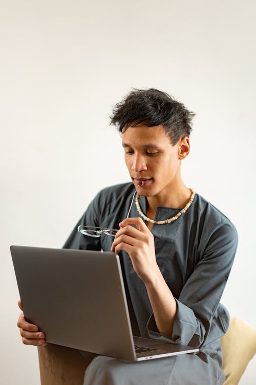 A Man Holding a Pair of Eyeglasses While Using a Laptop