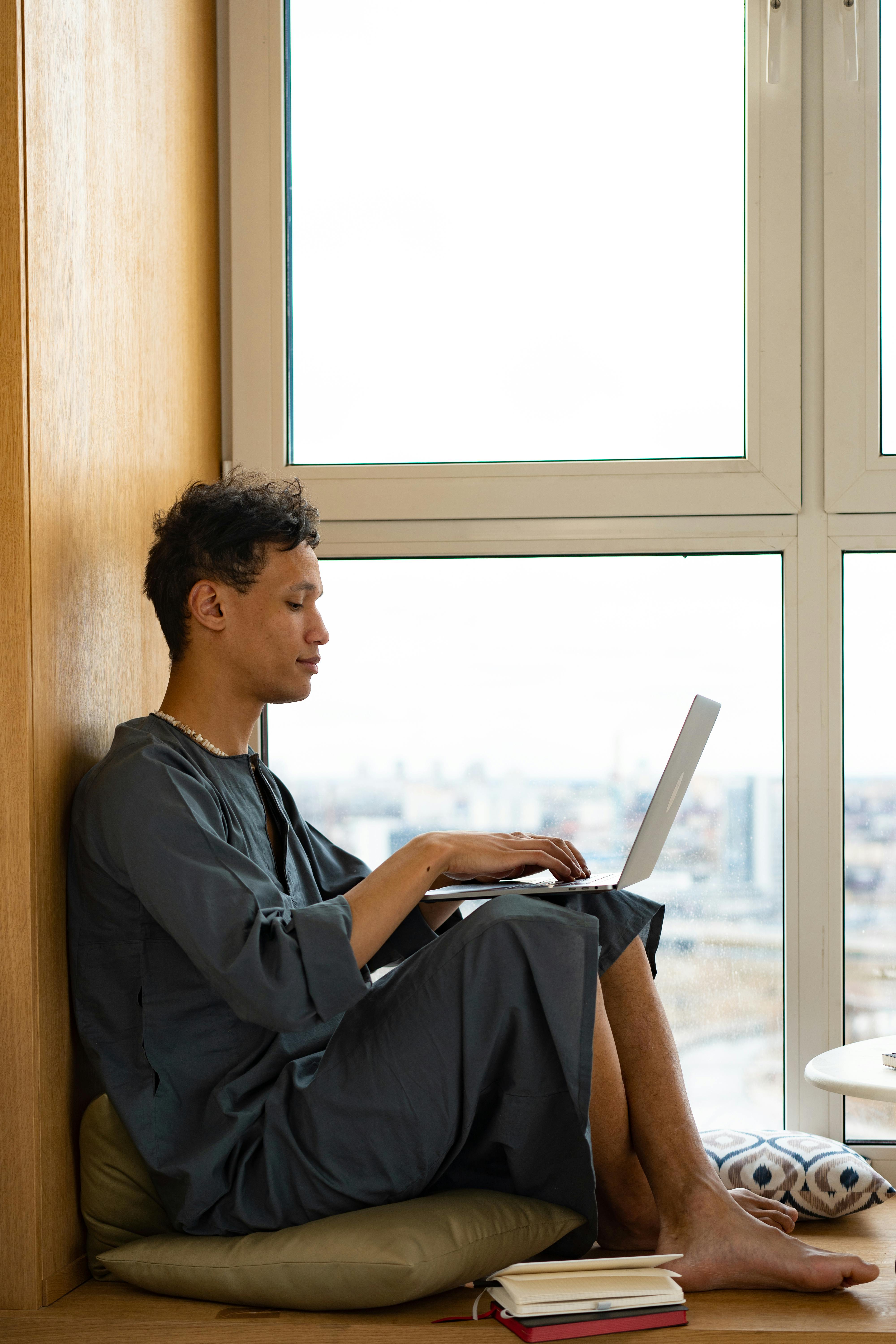 a man typing on laptop by the window