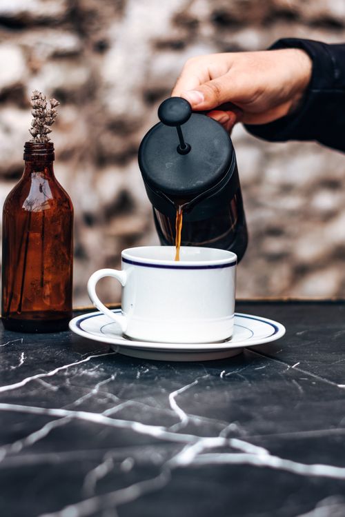 Free Close-up of coffee being poured into a cup from a French press on a marble table outdoors. Stock Photo