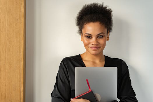 Confident woman indoors holding a laptop and smiling warmly.