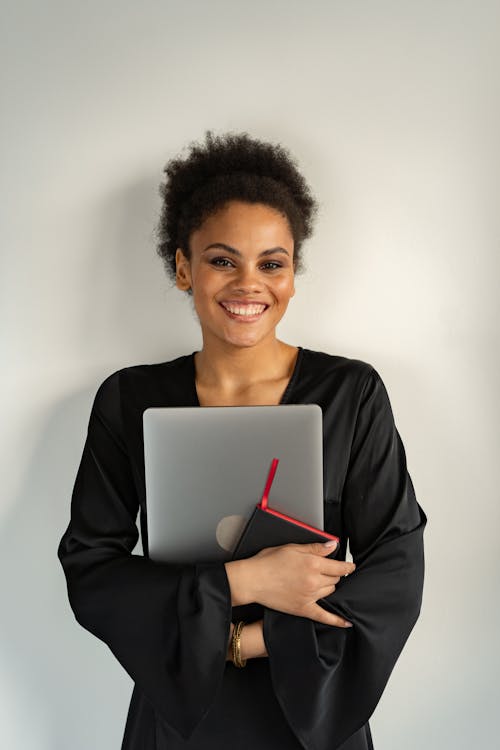 Smiling Woman in Black Long Sleeve Dress Holding a Silver Laptop
