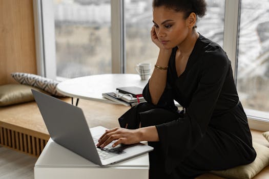 Woman focused on remote work with a laptop in a modern indoor setting, displaying concentration and productivity.