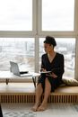 A Woman Holding a Notebook while Looking at a Laptop