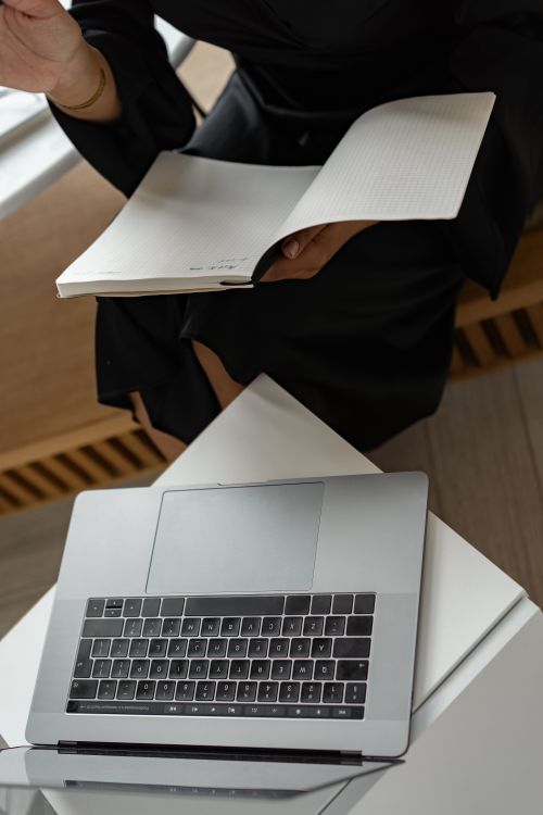 Free A woman multitasks with a laptop and notebook, symbolizing online education and productivity. Stock Photo