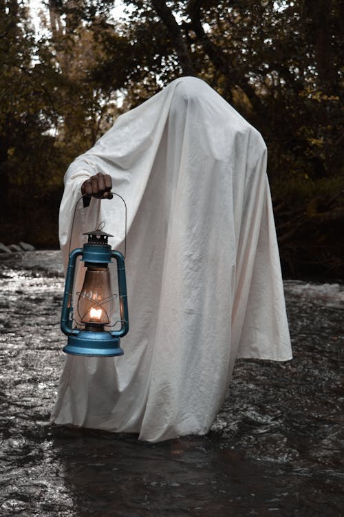 A Person Under a White Blanket Holding an Oil Lamp
