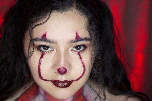 A striking close-up portrait of a woman with clown makeup and a red background, perfect for Halloween themes.
