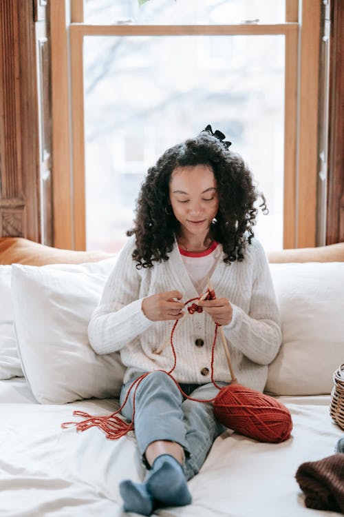 Focused African American woman knitting on bed