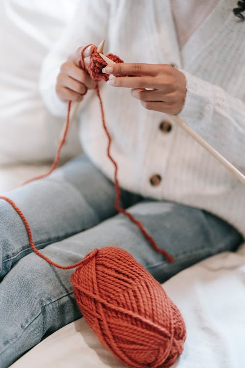 Unrecognizable woman knitting with needles on bed