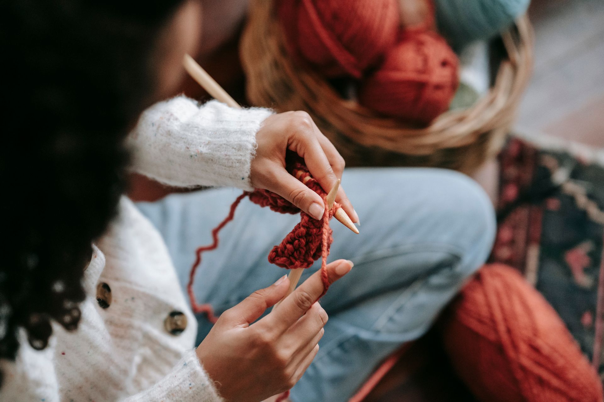 A woman knitting with red yarn, surrounded by a cozy indoor atmosphere and yarn basket.