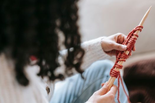High angle of crop anonymous female with dark curly hair in casual clothes casting on new stitches wooden needles while knitting warm clothes during weekend at home