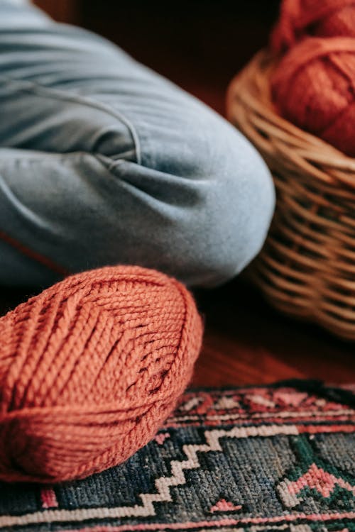 Crop woman sitting on floor and knitting with yarn