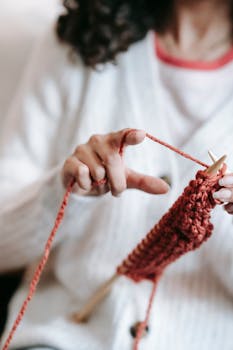 Crop anonymous with curly dark hair tying woolen thread on finger while knitting with yarn and needles at home