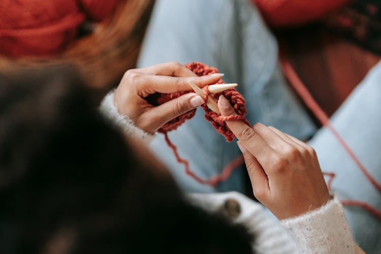 Anonymous Lady Knitting Warm Scarf With Red Yarn And Needles