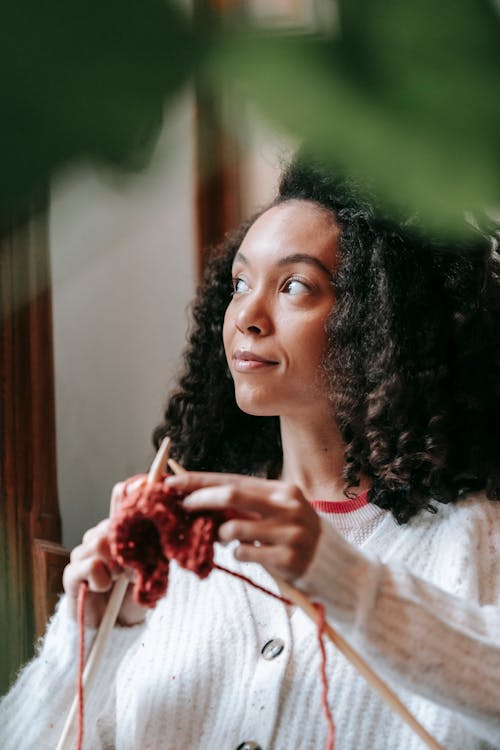 Dreamy young ethnic woman creating knitwear at home