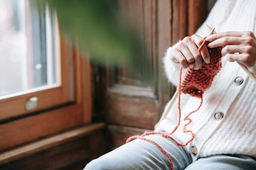 Crop anonymous lady sitting near window and knitting during weekend at home