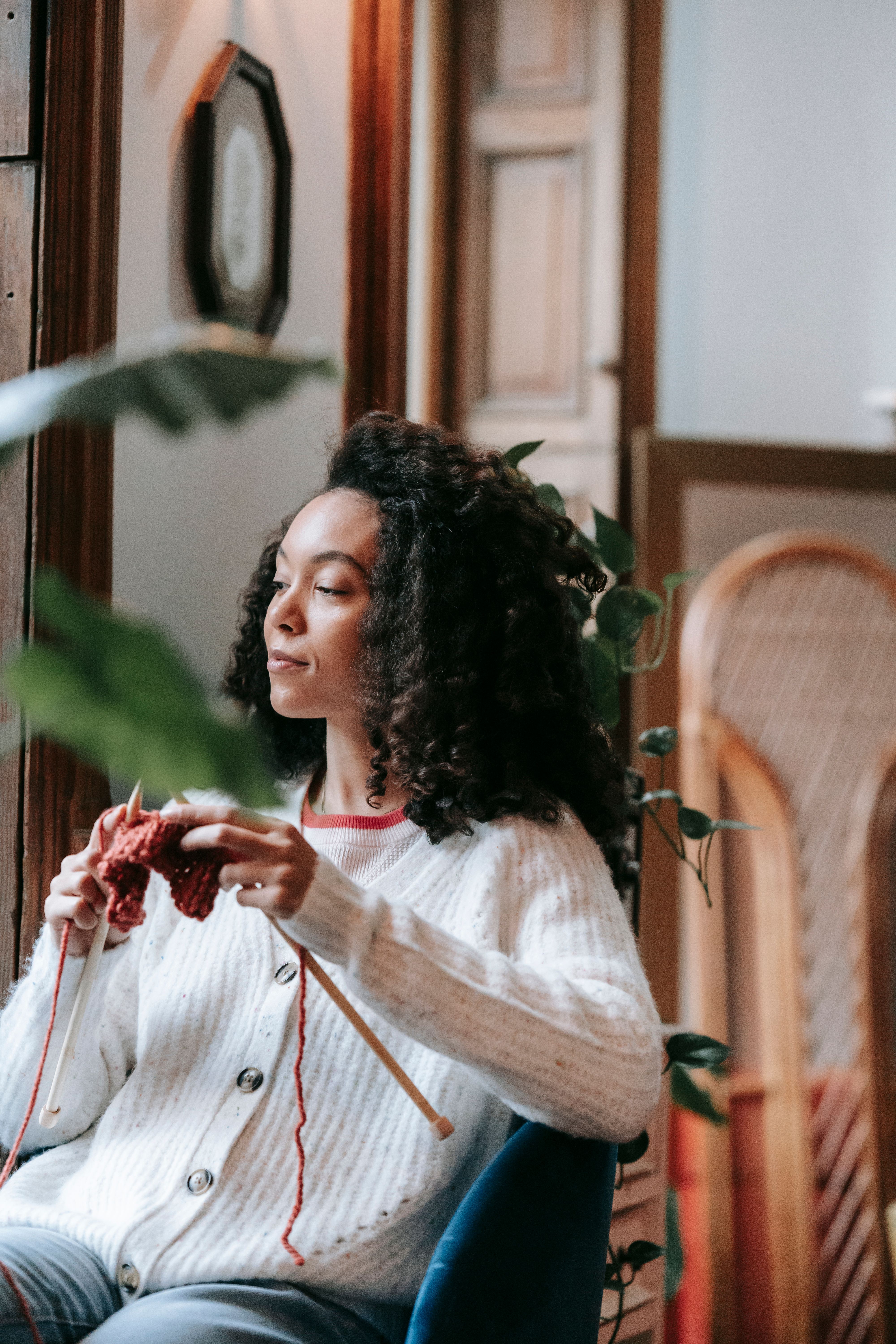 Relaxed woman knitting a red sweater, showcasing calmness in a cozy indoor environment.