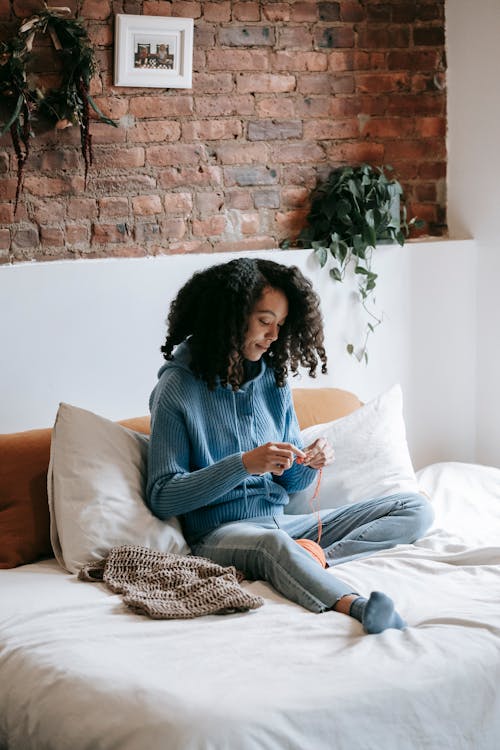 Free A Woman in Knitted Sweater Sitting on the Bed while Crocheting Stock Photo