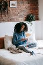 A Woman in Knitted Sweater Sitting on the Bed while Crocheting