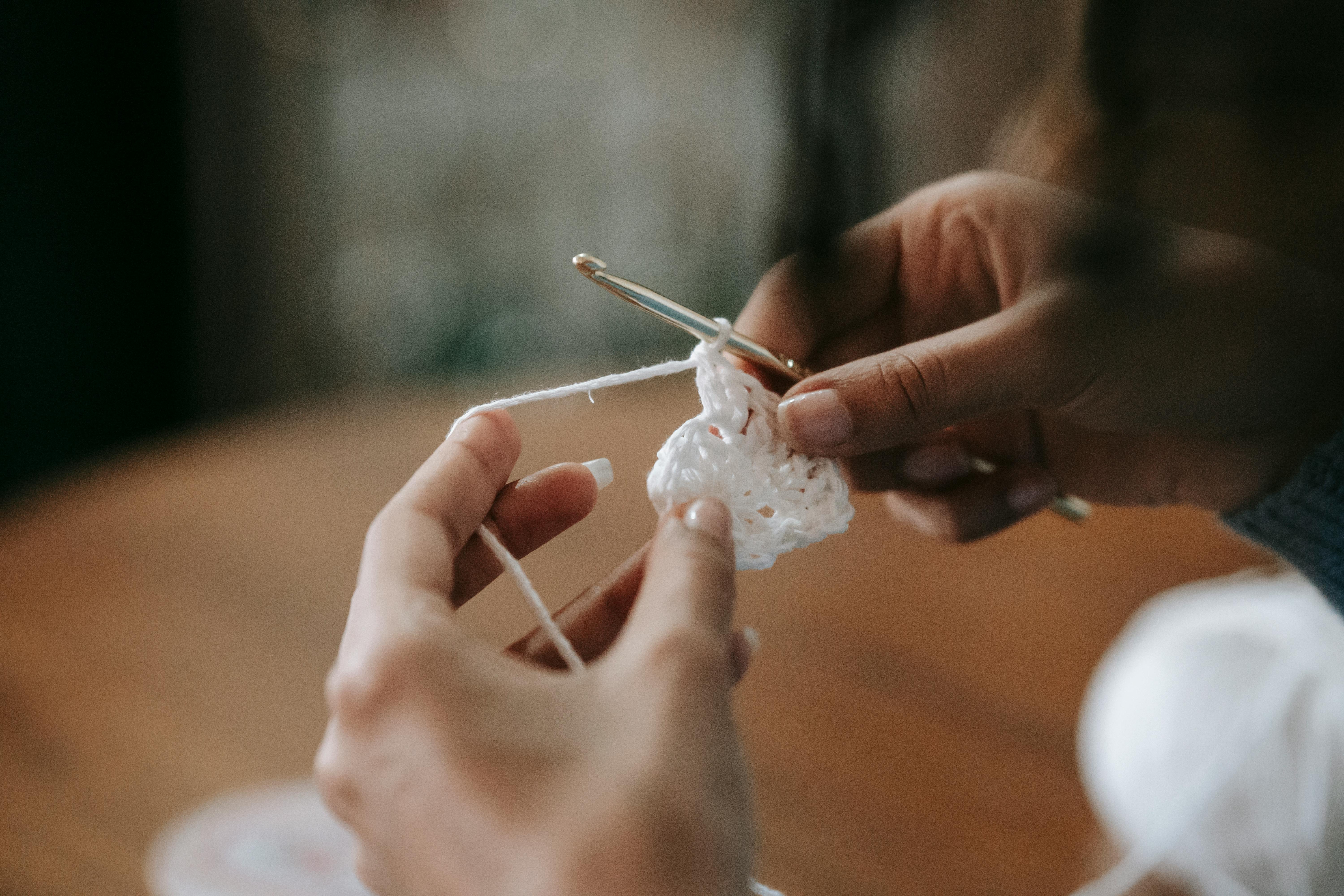 Detailed close-up of hands crocheting with a crochet hook and white yarn.