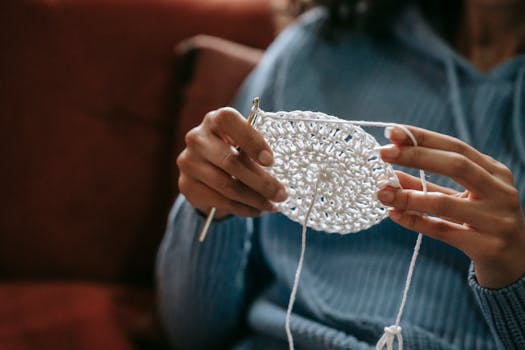 Close-up of a woman crocheting with white yarn in a comfortable indoor environment.
