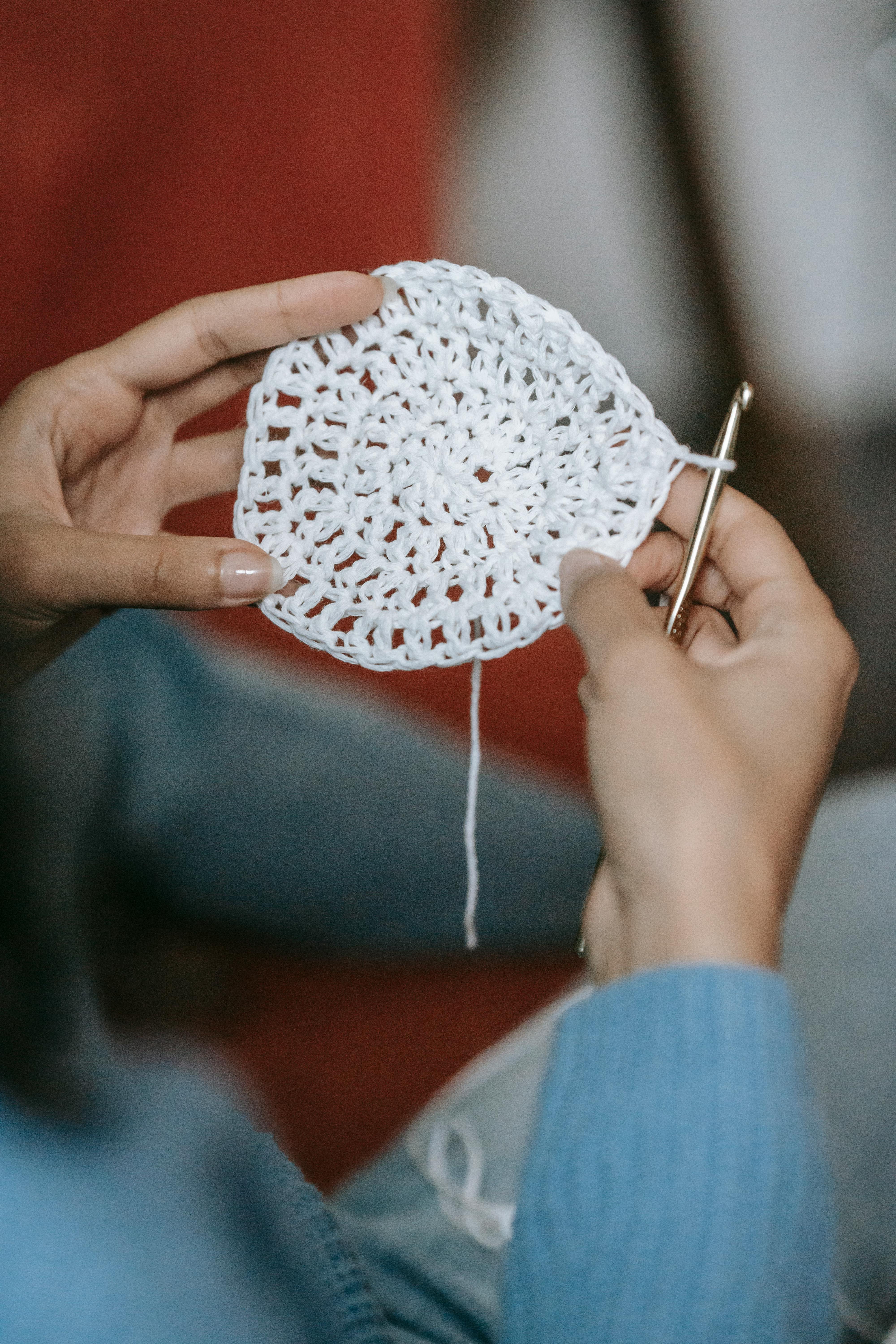 Detailed view of hands crocheting a white textile, emphasizing DIY craft techniques.