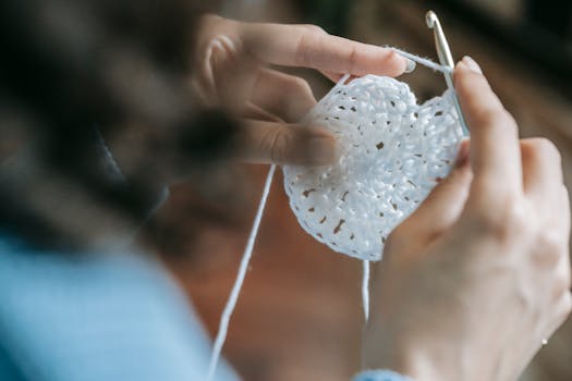 Detailed view of hands crocheting with white yarn, showcasing craftsmanship and texture.