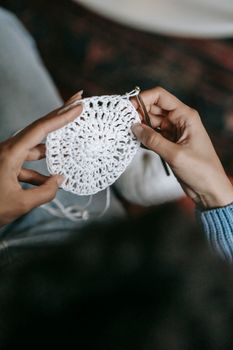 Detailed close-up of hands expertly crocheting a white textile with a crochet hook.