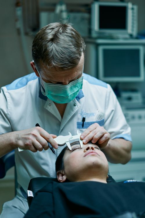 Free A surgeon measures a patient's eyelids with calipers in a medical clinic, preparing for a procedure. Stock Photo