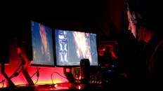 在光线昏暗的房间里，一名男子正全神贯注地盯着多台电脑显示器，展现了高科技的工作环境