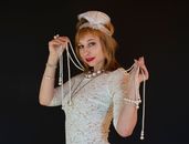Attractive female model in twenties style dress and headpiece with feather looking at camera while touching beads on black background