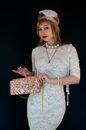 Charming female model in retro style dress and headpiece with feather looking at camera with sequin handbag on black background