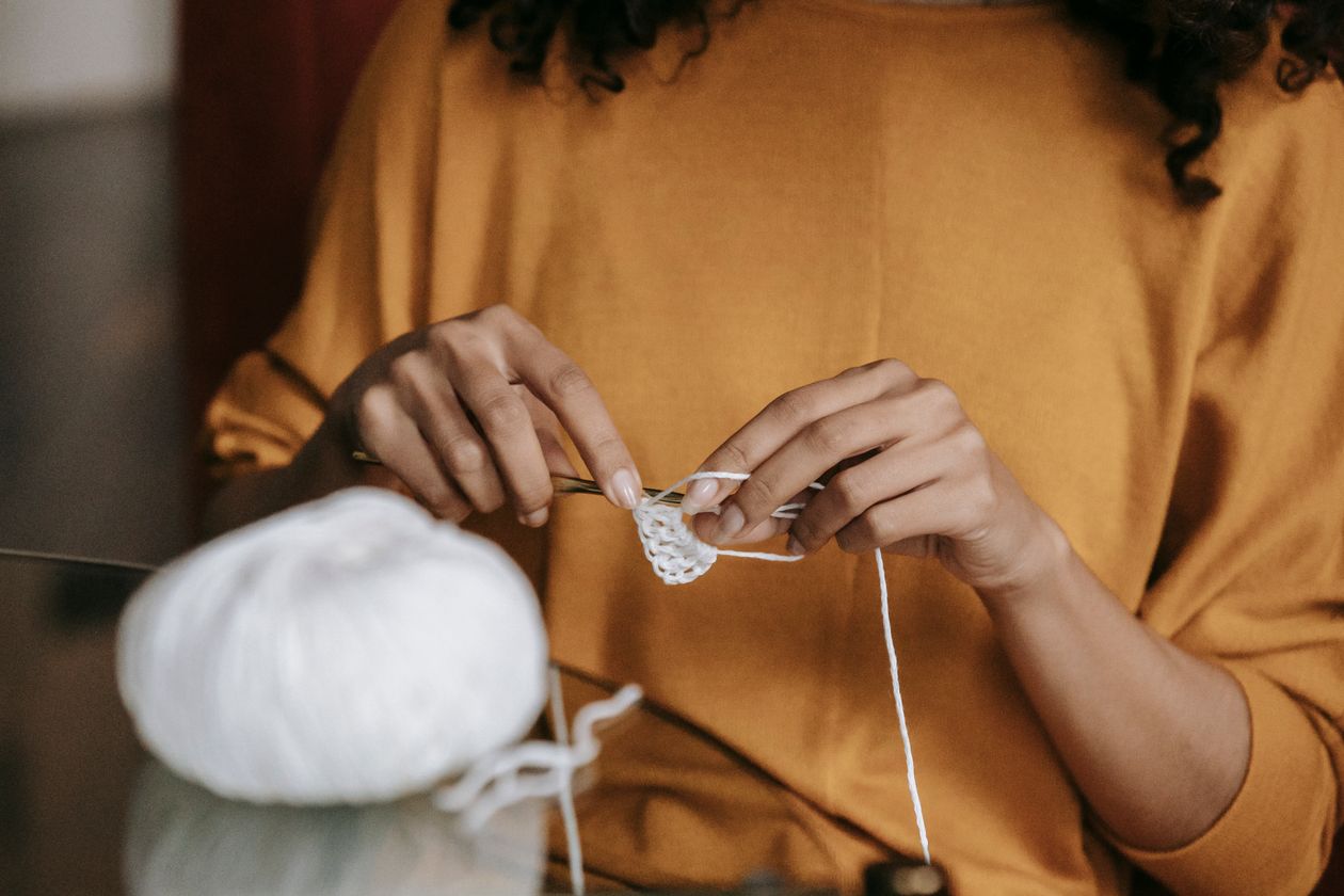 Mãos aprendendo crochê com agulha e fio branco