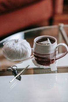 A warm cup of tea with knitting supplies on a glass table, perfect for a cozy indoor setting.