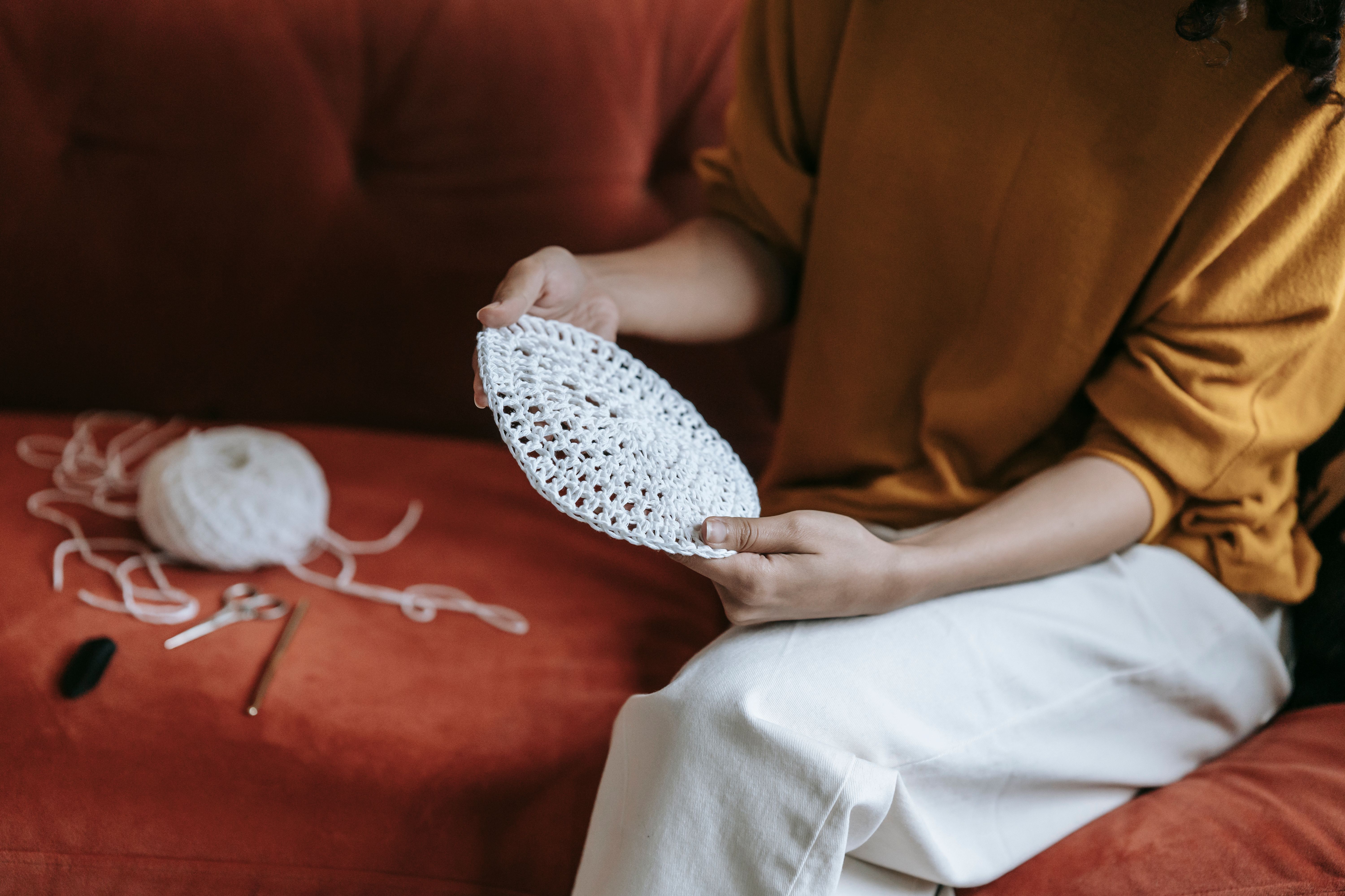 A woman sits on a red sofa crochet stitching a white pattern, evoking warmth and creativity related to how to crochet complex
