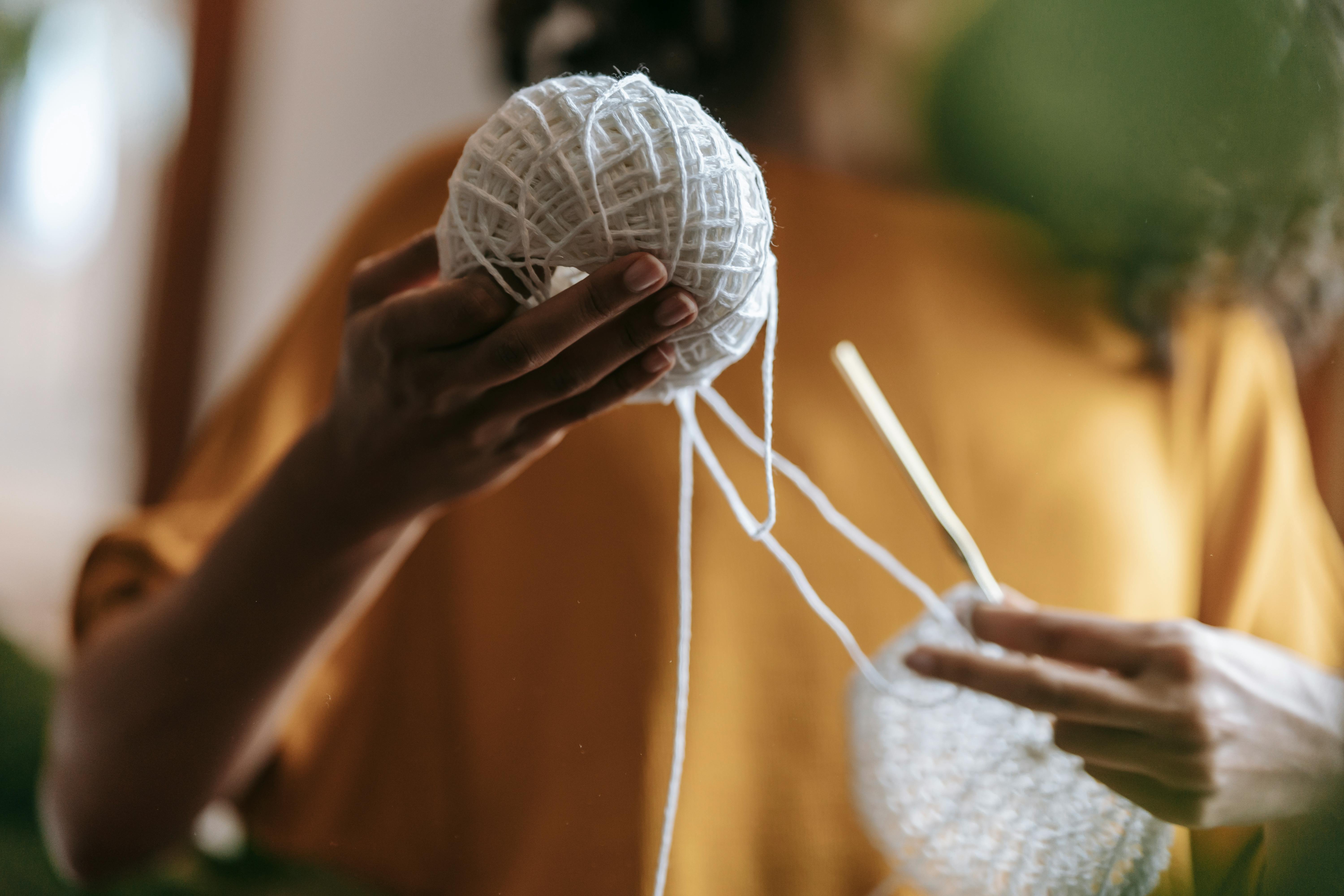 Close-up of a woman crocheting with white yarn and crochet hook indoors.