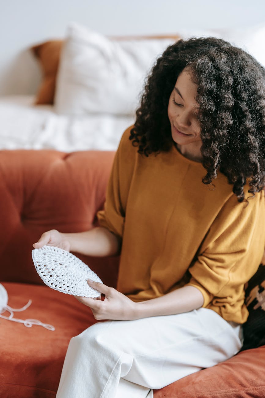African American woman crocheting on a rust-colored sofa, showcasing a relaxed lifestyle.