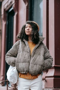Contemplative young African American female in stylish outerwear with hands in pockets looking away in town