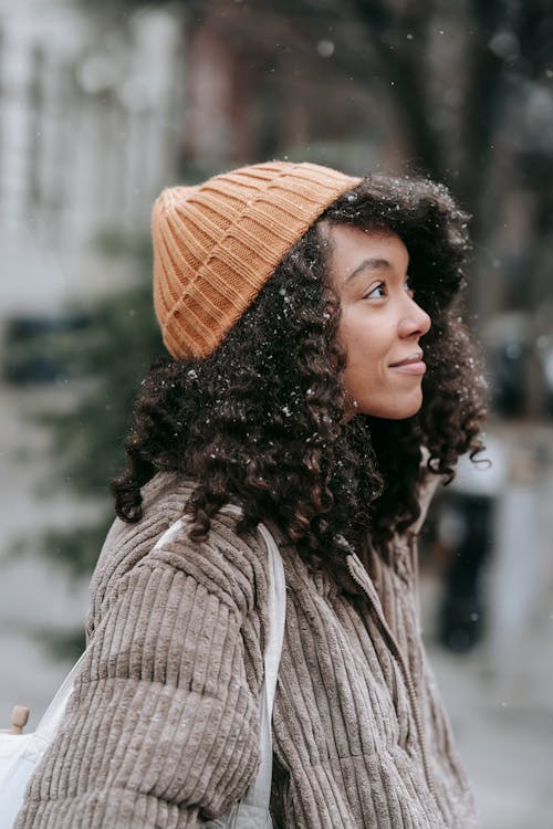 Contemplative ethnic woman with curly hair in snowfall