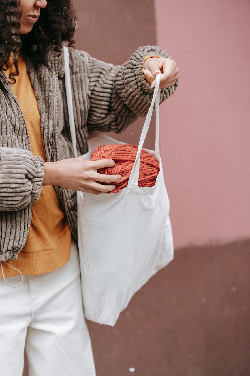 Woman placing skein of yarn into eco-friendly cotton tote bag, highlighting sustainable fashion and zero waste lifestyle.