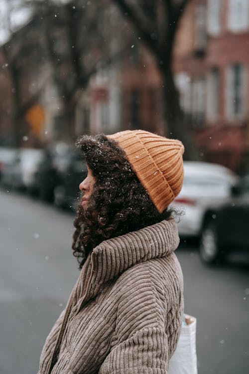 Side view of African American female with Afro hairstyle in knitted hat on urban road in wintertime