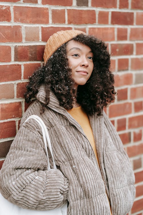 Dreamy young black female in warm clothes with hand in pocket looking away on winter street