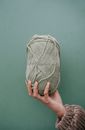 Crop unrecognizable female reaching out hand and demonstrating ball of yarn against green background