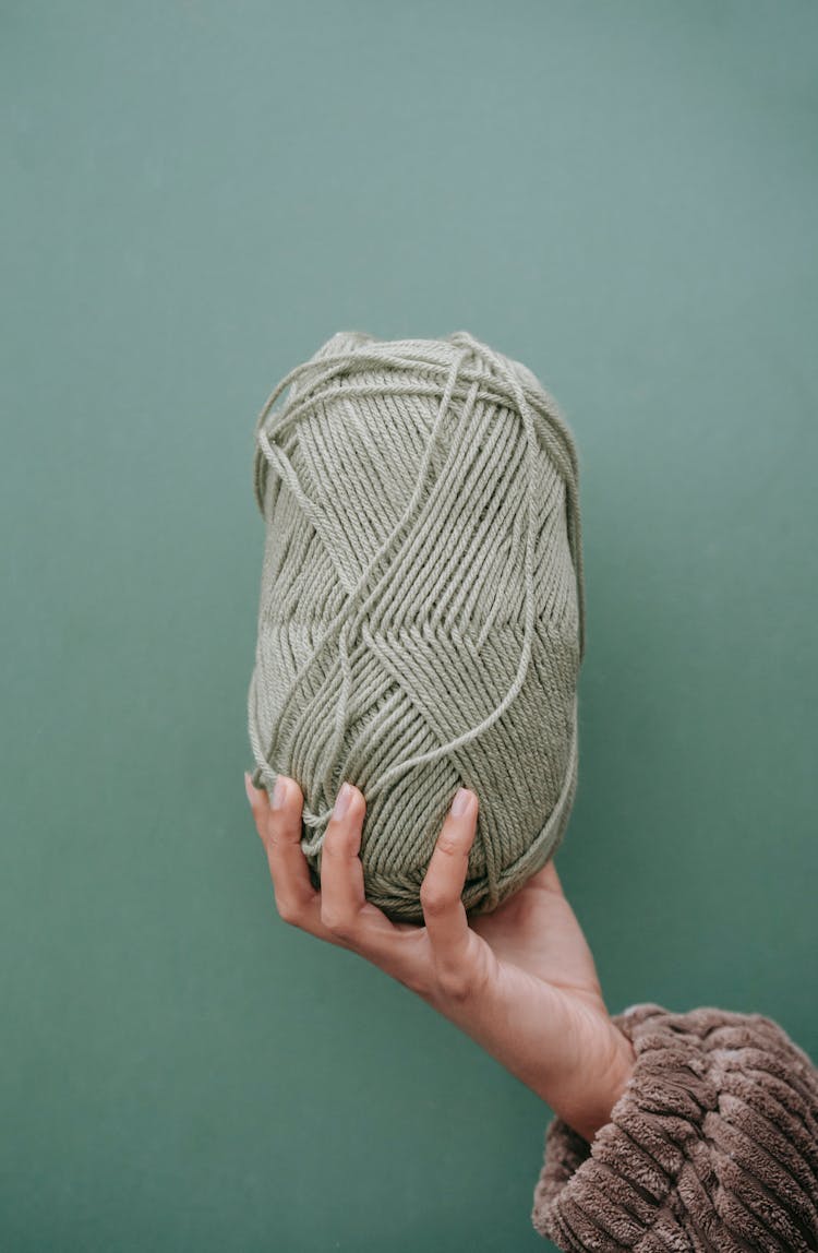 Woman Showing Ball Of Yarn Against Green Background