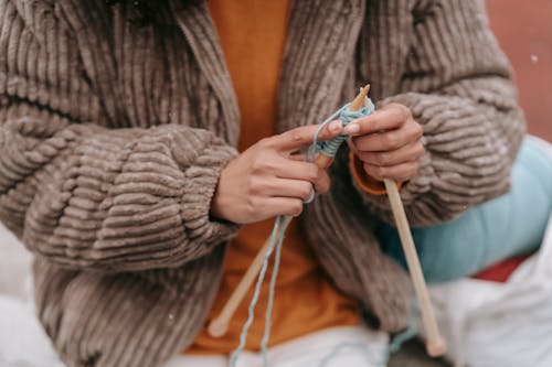 Female in stylish outerwear knitting on street in daylight